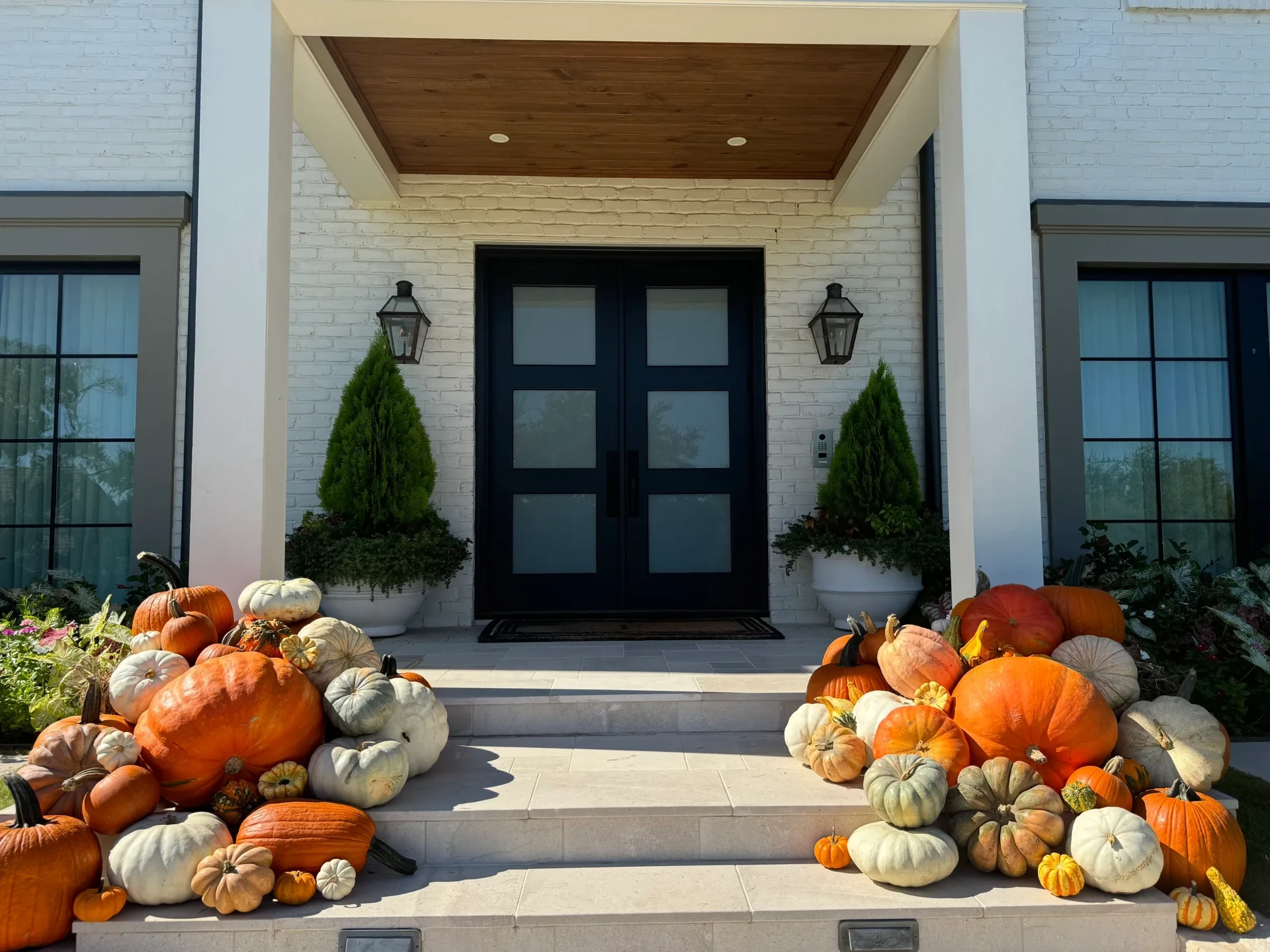 Large fall porch display of orange and heirloom pumpkins beside a black double door